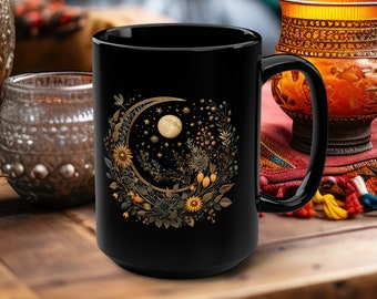 May include: Black ceramic mug with a crescent moon and floral design. The moon is surrounded by stars and flowers in shades of gold and yellow.