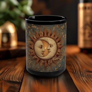 Könnte beinhalten: Schwarze Keramiktasse mit einem Vintage-Design, das eine Sonne und einen Mond mit Gesichtern zeigt. Die Sonne hat eine goldgelbe Farbe und der Mond ist eine Sichelform mit hellblauer Farbe. Der Hintergrund ist blau und grün mit floralen Details.