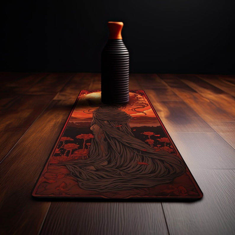 May include: A yoga mat with a red, orange, and black design featuring a woman in a flowing robe. The mat is on a wooden floor with a black bottle standing on top of it.