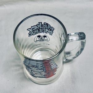 May include: Clear glass mug with a handle, featuring the text "Mickey Mouse" in a stylized font. The mug has a ribbed design and a graphic of Mickey Mouse. The design is in black, red, and white.