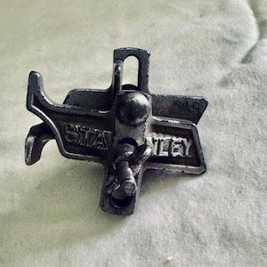 May include: A vintage metal Stanley clamp, featuring the brand name prominently displayed. The clamp has a complex design with a lever and screw mechanism, showing signs of wear and age. The tool is likely used for woodworking or construction.