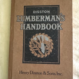 Könnte beinhalten: Ein Vintage "Lumberman's Handbook" von Henry Disston & Sons, Inc. Das Cover ist hellbraun mit schwarzem Text und einer kreisförmigen Grafik einer Sägeblatt und Holzfällern. Der Titel des Buches ist fett gedruckt.