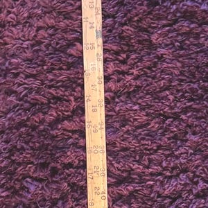 May include: A vintage wooden ruler with metal end caps, measuring up to 52 inches. The ruler is marked with inch increments and numbers, and has a light wood handle. The ruler is set against a deep purple background.