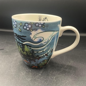 Könnte beinhalten: Ein Keramikbecher mit einer blau gehaltenen Landschaftsillustration, die einen stilisierten weißen Adler, einen Vollmond, Nadelbäume und blaue Blumen zeigt. Am inneren Rand befindet sich eine kleine schwarze Grafik eines Tipis mit dem Text "SLAM".