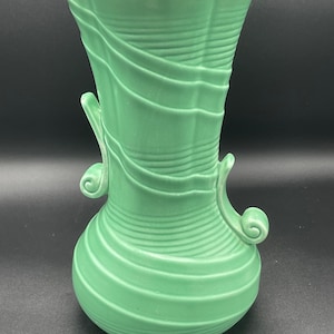 Könnte beinhalten: Eine grüne Keramikvase mit einem wirbelnden, strukturierten Design und zwei Griffen. Die Vase hat eine breite Öffnung und einen abgerundeten Boden.