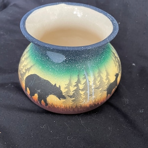 May include: A ceramic vase with a green, yellow and brown woodland scene. The vase features a silhouette of a bear and a deer in the forest.