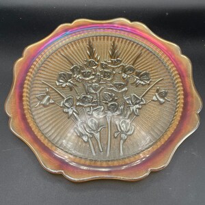 May include: A vintage iridescent glass plate with a scalloped edge and a floral design. The plate is in shades of amber and red.