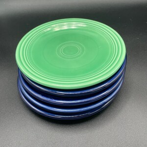 May include: A stack of four ceramic plates, two green and two blue. The top plate is green with a white rim and the bottom plate is blue with a white rim.