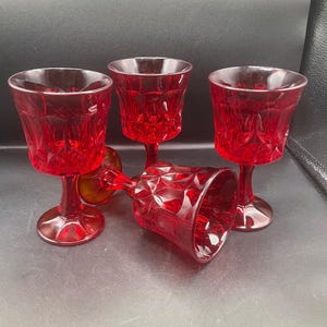 Può includere: Quattro calici rossi rubino con un motivo a diamante. Tre calici sono in posizione verticale, mentre uno è sdraiato su un lato. I calici hanno un design classico e sono in vetro trasparente.