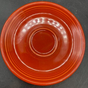 May include: A red ceramic saucer with a slightly raised centre. The saucer has a glossy finish and a simple design.