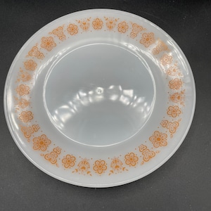 May include: A white ceramic dinner plate with a brown floral pattern around the rim.