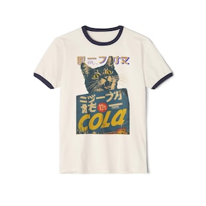 May include: A white t-shirt with a navy blue ringer. The shirt features a vintage-style graphic of a black cat holding a blue and yellow box with Japanese text that reads "Cola" and "Drink Cola".