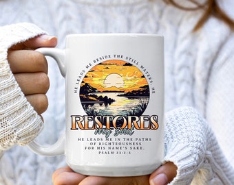 May include: White ceramic mug with a colorful sunset scene and the text "He leads me beside the still waters. He restores my soul. He leads me in the paths of righteousness for His name's sake. Psalm 23:2-3"