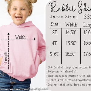 Puede incluir: Sudadera con capucha rosa con una tabla de tallas que muestra las medidas de ancho y largo en pulgadas. La tabla muestra las tallas 2T, 4T y 5-6T. La sudadera est&aacute; hecha de 60% algod&oacute;n peinado ring-spun y 40% poli&eacute;ster. Tiene construcci&oacute;n de costuras laterales con bolsillos laterales, pu&ntilde;os y cintura de punto acanalado, y hombros y sisas con pespuntes.