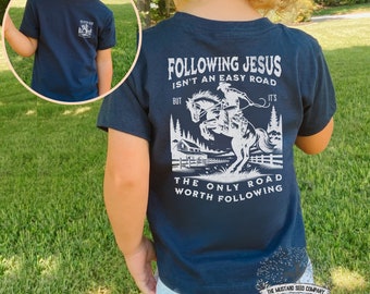 May include: Navy blue short-sleeved t-shirt with a white graphic of a cowboy riding a horse. The graphic includes the text "Following Jesus isn't an easy road, but it's the only road worth following".