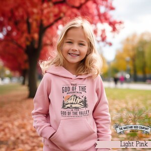 Puede incluir: Una sudadera con capucha de color rosa claro con un dise&ntilde;o gr&aacute;fico que presenta una monta&ntilde;a y el texto "The God of the Mountain is the God of the Valley".