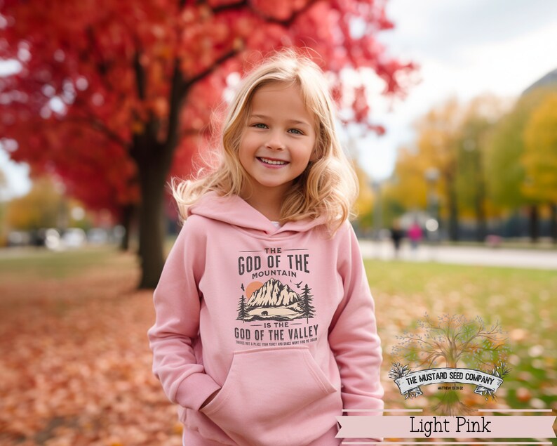 Puede incluir: Una sudadera con capucha de color rosa claro con un dise&ntilde;o gr&aacute;fico que presenta una monta&ntilde;a y el texto "The God of the Mountain is the God of the Valley".