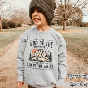 May include: A gray sweatshirt with a vintage-style graphic design featuring a mountain range, a bear, and the text "The God of the Mountain is the God of the Valley. There's not a place your mercy and grace won't find me again."