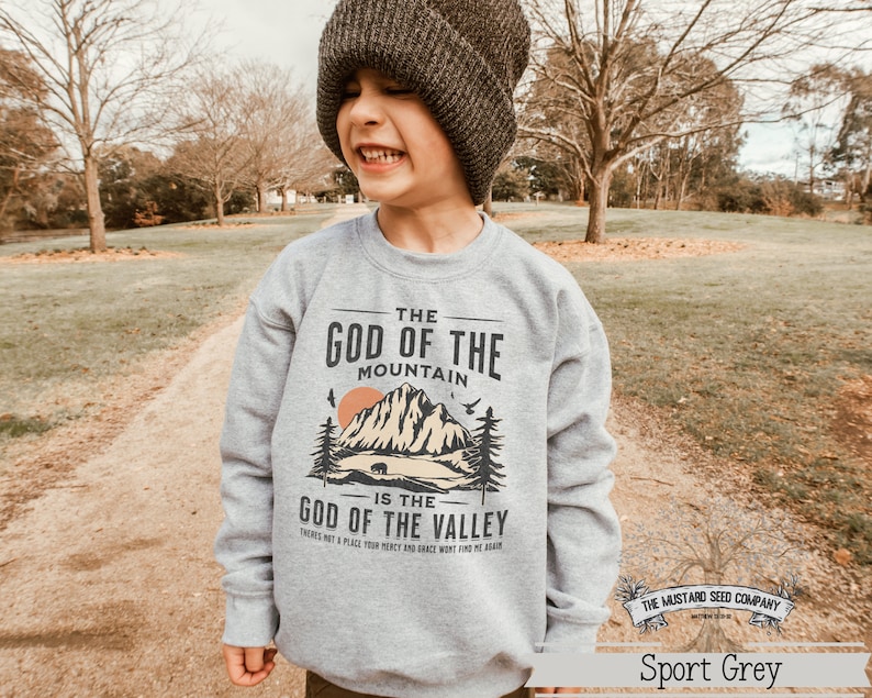 May include: A gray sweatshirt with a vintage-style graphic design featuring a mountain range, a bear, and the text "The God of the Mountain is the God of the Valley. There's not a place your mercy and grace won't find me again."