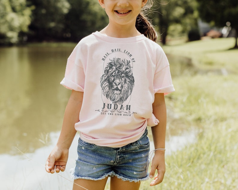 May include: A pink t-shirt with a black and white lion graphic and the text "Hail Lion of Judah Let the Lion Roar".