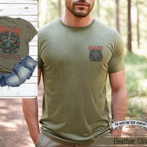 May include: A green t-shirt with a graphic print of a sword and the text "Let Us Hold Fast" on the back. The front of the shirt has a smaller version of the graphic print. The shirt is made by The Mustard Seed Company and the text "Matthew 6:33" is printed below the company name.
