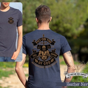 May include: Heather navy blue t-shirt with a gold graphic of a knight in armor with the text "Put on the Full Armor of God and Stand Against the Devil's Schemes" and the text "The Mustard Seed Company" at the bottom.