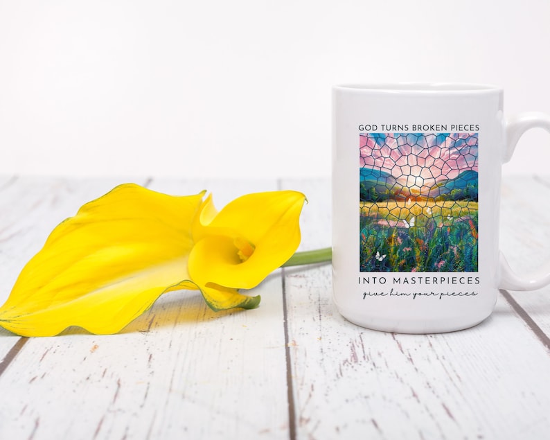 Pu&ograve; includere: Tazza in ceramica bianca con un'immagine colorata in stile vetrata di un tramonto su un campo. Il testo "God turns broken pieces into masterpieces give him your pieces" &egrave; stampato sulla tazza.