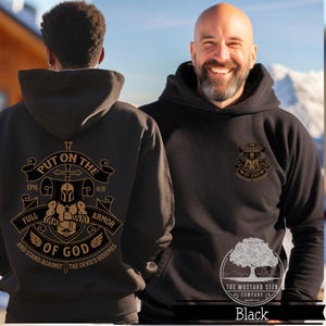 May include: Black hoodie with a gold graphic on the front and back. The graphic features a knight in armor with a sword and the text "Put on the Full Armor of God" and "Eph. 6:11". The back of the hoodie has the text "And stand against the devil's schemes".