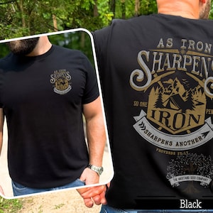 May include: Black t-shirt with a gold graphic design that says "As Iron Sharpens Iron" with a camping scene and the text "So One Person Sharpens Another Proverbs 27:17" and the company logo "The Mustard Seed Company".
