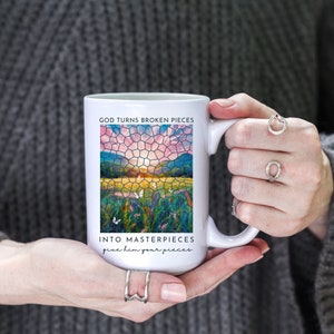 Pu&ograve; includere: Tazza in ceramica bianca con un design a mosaico di vetro colorato di un tramonto su un campo. Il testo "GOD TURNS BROKEN PIECES INTO MASTERPIECES give him your pieces" &egrave; stampato sulla tazza.