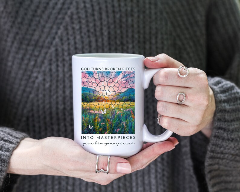 Pu&ograve; includere: Tazza in ceramica bianca con un design a mosaico di vetro colorato di un tramonto su un campo. Il testo "GOD TURNS BROKEN PIECES INTO MASTERPIECES give him your pieces" &egrave; stampato sulla tazza.