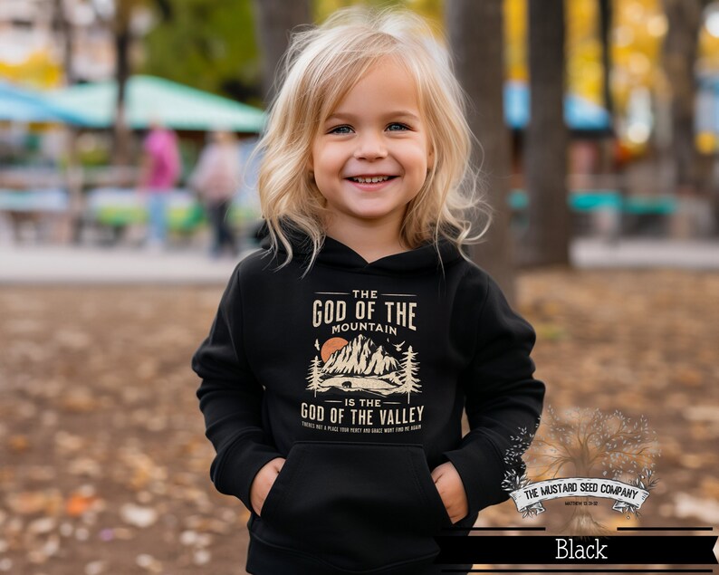 Puede incluir: Una sudadera con capucha negra con un estampado gr&aacute;fico de una cordillera y el texto "The God of the Mountain is the God of the Valley".