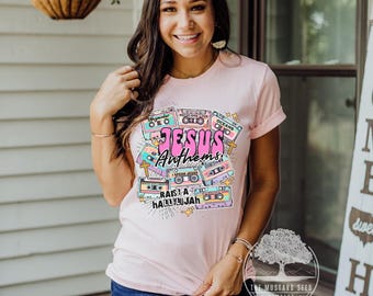 May include: A pink t-shirt with a graphic design of cassette tapes with the text "Jesus Anthems" and "Raise a Hallelujah".