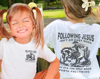May include: White t-shirts with the text "Following Jesus Isn't An Easy Road" and a graphic of a person riding a horse. The shirts also have the text "But It's The Only Road Worth Following".