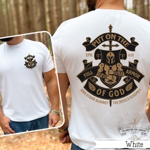 May include: White t-shirt with a black and gold graphic design featuring a knight in armor with a sword and the text "Put on the Full Armor of God" and "Eph. 6:11" and "And Stand Against the Devil's Schemes".