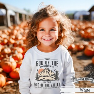 May include: White sweatshirt with a graphic design of a mountain and a bear. The text on the sweatshirt reads "The God of the Mountain is the God of the Valley".