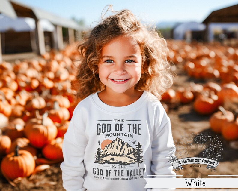 May include: White sweatshirt with a graphic design of a mountain and a bear. The text on the sweatshirt reads "The God of the Mountain is the God of the Valley".