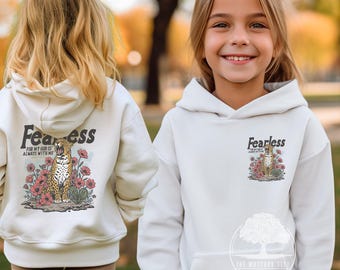 May include: White hoodie with the word "Fearless" above a graphic of a leopard surrounded by pink flowers. The text "FOR MY GOD IS ALWAYS WITH ME" is below the leopard. The hoodie is shown on a young person.