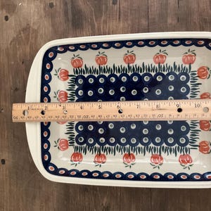 May include: Rectangular ceramic serving dish with a white rim and a blue and red floral pattern. The dish is approximately 12 inches long. The interior features a blue and white dotted design with red floral accents.