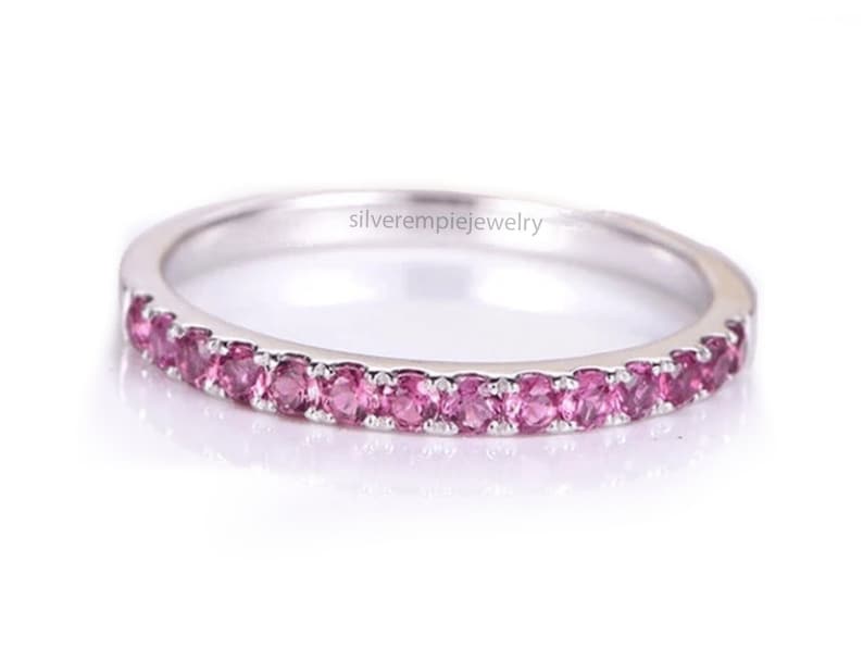 May include: A delicate silver band ring with a row of pink gemstones. The ring is simple and elegant, perfect for everyday wear.