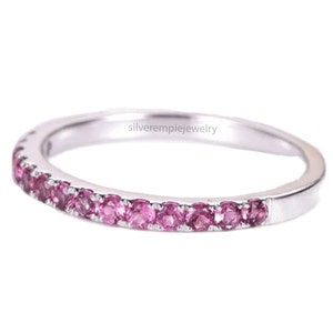 May include: A delicate silver band ring with a row of pink gemstones set around the entire band. The ring is a simple and elegant design.