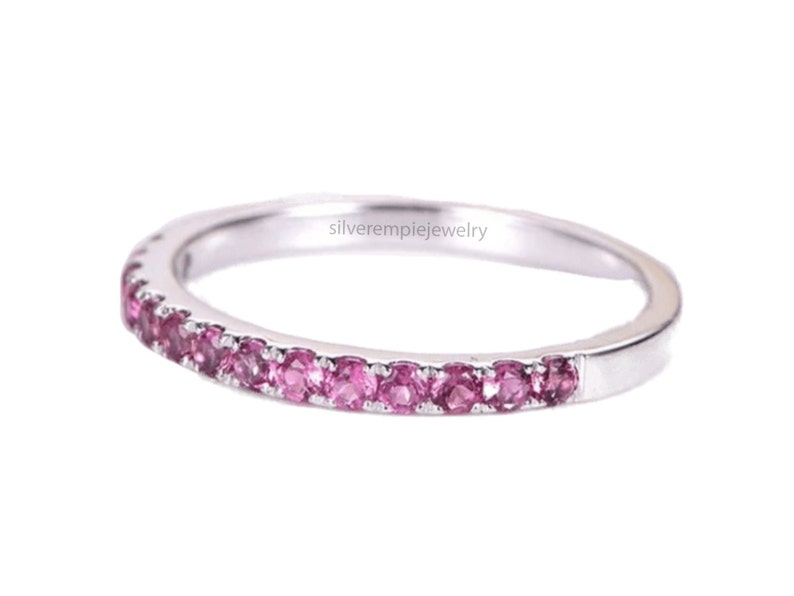 May include: A delicate silver band ring with a row of pink gemstones set around the entire band. The ring is a simple and elegant design.