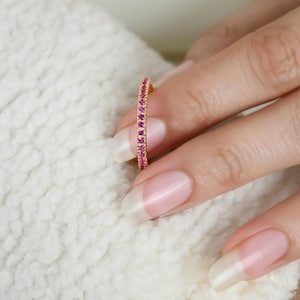 Könnte beinhalten: Ein dünner Goldring mit einer Reihe kleiner rosafarbener Edelsteine.