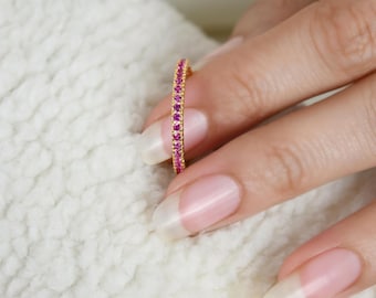 May include: A thin gold band ring with a row of small pink gemstones.