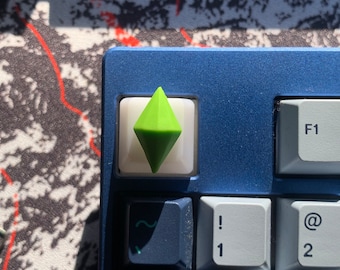 May include: A green diamond-shaped keycap for a mechanical keyboard. The keycap is on a blue keyboard with white keys.