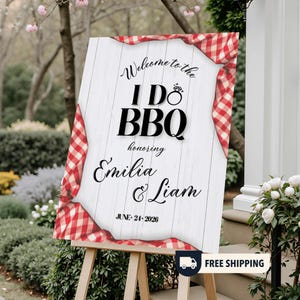 May include: A wooden sign on an easel with the text "Welcome to the I Do BBQ honoring Emilia & Liam June 24, 2026." The sign has a white background with a red and white checkered border.