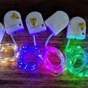 May include: A collection of battery-operated LED string lights in various colors, including blue, green, pink, and yellow. Each light strand is connected to a white battery pack with a safety symbol.