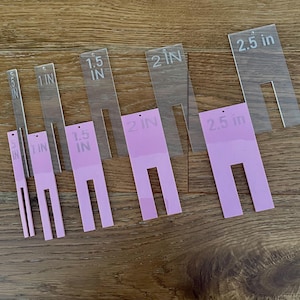 May include: Six acrylic templates for crafting, with measurements in inches. The templates are clear and pink, with cut-out shapes for creating projects.