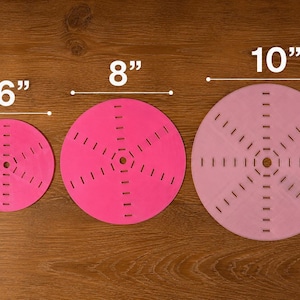 May include: Three pink circular craft tools, 6", 8", and 10" in diameter, with radial slots and a central hole. The tools are arranged on a wooden surface, showcasing their graduated sizes for crafting projects.