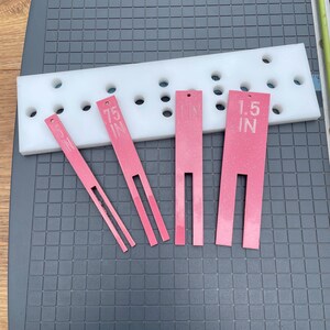 May include: A white plastic guide with multiple holes and four pink tools. The tools are labeled with measurements of 1.5 IN and 0.75 IN. The tools have a slotted design.